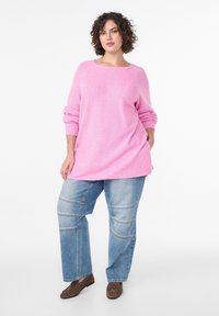 Svetloružový pletený sveter s voľnými, dlhými rukávmi a okrúhlym výstrihom, skombinovaný so svetlomodrými džínsami s širokými nohavicami a panelovým detailom.