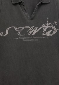 Gray cotton polo shirt with a V-neck and short sleeves, featuring a stylized logo and text on the front. Durable fabric with a textured finish.