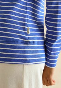 Modrá a biela pruhovaná košeľa s dlhým rukávom vyrobená z bavlny. Obsahuje štítok s logom "Joules" na bočnom šve a má jemnú textúru.