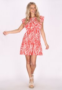 Rochie cu model floral roșu și alb, cu mâneci volănașe, talie strânsă și fustă evazată. Asortată cu sandale cu barete de culoare deschisă.