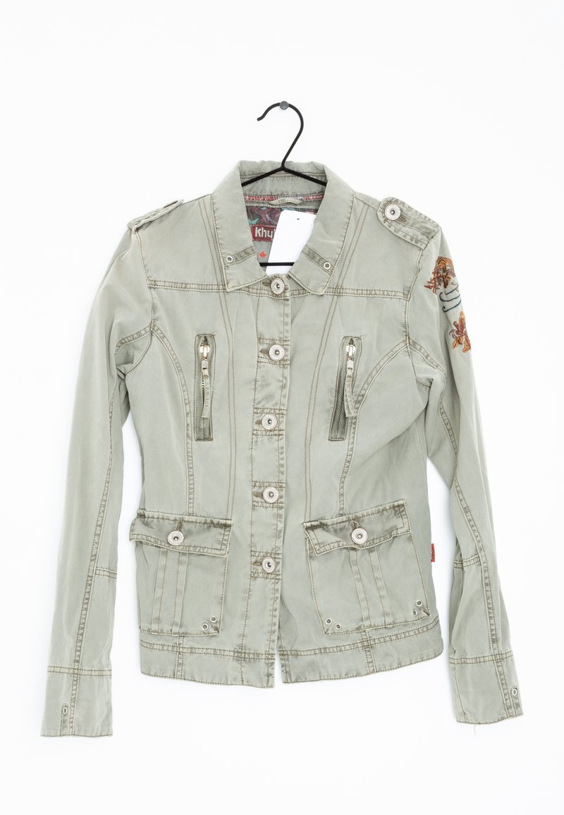 Giacca verde oliva con maniche lunghe, chiusura frontale con bottoni, due tasche con cerniera e spalline. Caratterizzata da un ricamo decorativo sulla manica.