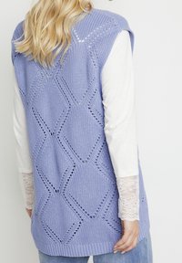 Licht paarse gebreide vest met een ruitpatroon, openweefdetails en een geribde zoom. Draagt over een wit langemouwen top met kantaccenten.