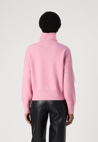 Rosa, flauschiger Pullover mit hohem Kragen, übergroßen Ärmeln und geripptem Saum, kombiniert mit schwarzen Kunstlederhosen.