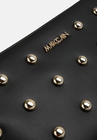 Black leather handbag featuring gold studs and a prominent metal logo, with a smooth texture and a structured design.