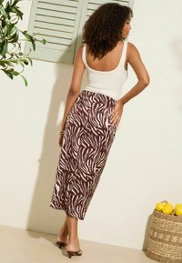 Bloemenprint rok in bruin en crème tinten, met een vloeiende ontwerp, een zachte textuur en een elastische tailleband. Gecombineerd met een aansluitend wit tanktop.