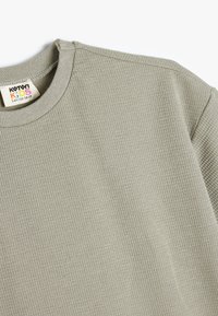 Sudadera gris de canalé con cuello redondo. Elaborada en suave algodón, presenta una textura sutil y una etiqueta que dice "Koton Kids."