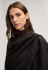 Zwarte sjaal van zacht, textuurstof, elegant gedrapeerd met een geribde, donkere halslijn. Subtiele stiksels langs de rand.