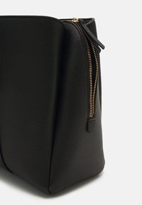 Sac en cuir noir texturé avec une fermeture éclair dorée, doté d'une forme structurée et d'une ouverture sur le dessus, idéal pour transporter les essentiels.