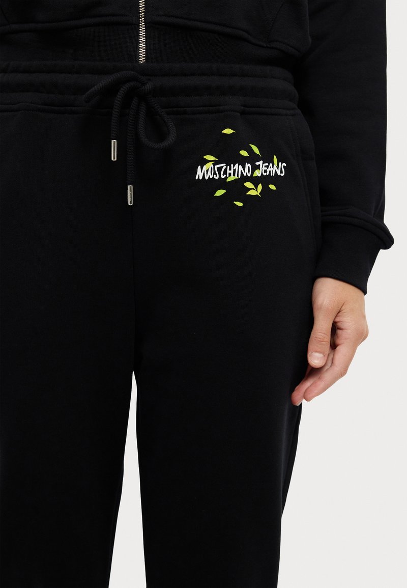 Schwarze Jogginghose aus Baumwollmischung, mit einem elastischen Bund und Kordelzug, sowie einem weißen Logo mit grünen Blattelementen am Oberschenkel.