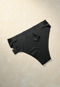 Black bikini briefs with a textured pattern, adjustable straps, and rectangular hardware accents. Smooth material and fitted design.