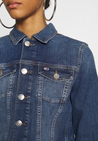 Jeansjacka i mörkblått med krage, silverknappar, bröstfickor och kontrasterande sömnadsdetaljer. Slät textur med en strukturerad passform.