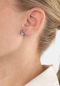 Pendientes de tono plateado con forma de símbolo del infinito retorcido, que presentan cristales claros brillantes y un acabado pulido.