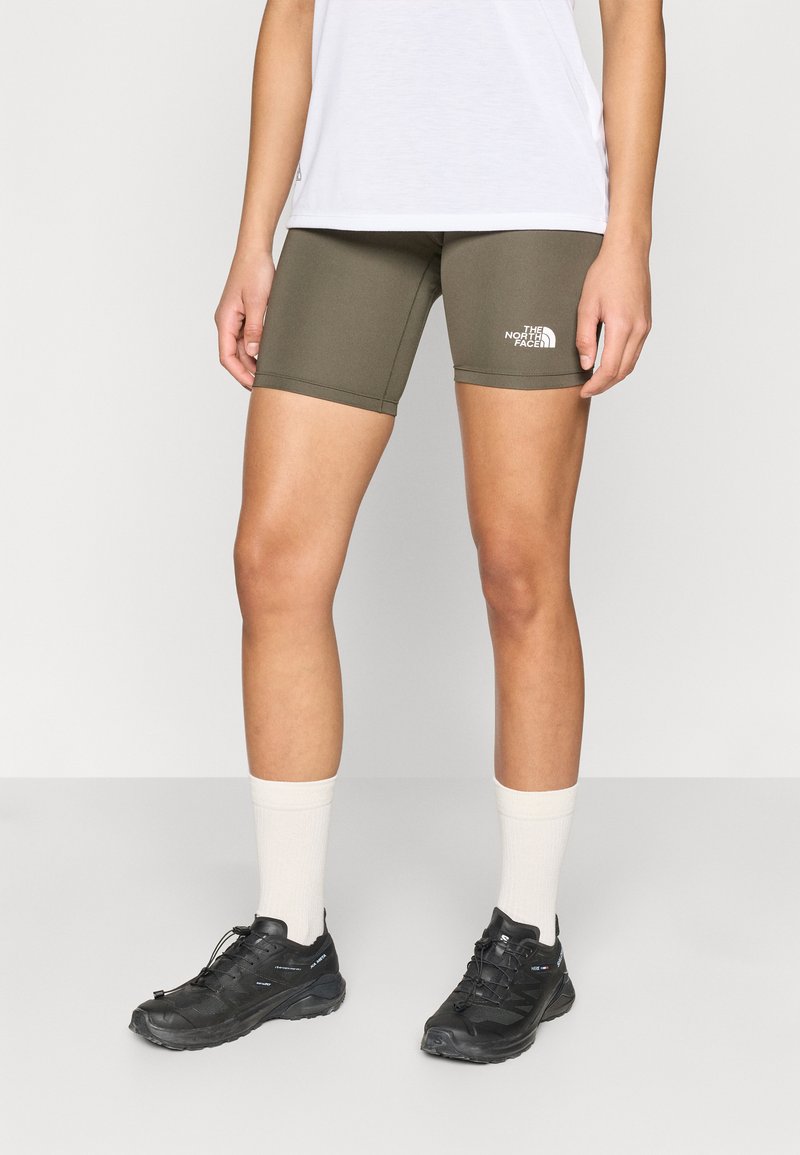 Βερμούδες ποδηλασίας σε ελαιόχρωμο πράσινο από ελαστικό ύφασμα, με λευκό λογότυπο. Συνδυάζονται με μαύρα αθλητικά παπούτσια και λευκές κάλτσες μεσαίου μήκους.