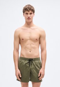 Ανδρικό μαγιό σορτς σε ελιά χρώμα με ελαστική μέση, κορδόνι για ρύθμιση και λεία υφή. Χωρίς ορατά σχέδια ή διακοσμήσεις.