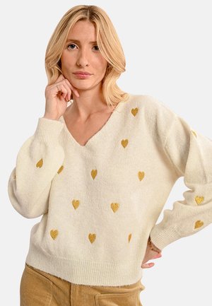 Maglione crema a V con motivi a cuori dorati, texture lavorata a maglia e maniche larghe con polsini e bordo a coste.
