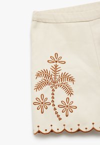 Beige tygkjol med intrikata bruna broderier av en palm och blommor, med en scalloped nederkant.