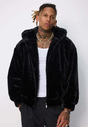 Veste zippée en fausse fourrure noire avec capuche, offrant une texture douce et une coupe décontractée. Comprend des poches latérales et des poignets côtelés.