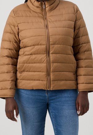 Hnědá prošívaná bunda na zip nošená přes modré džíny, zobrazena od ramen k bokům na osobě s tmavou pokožkou.