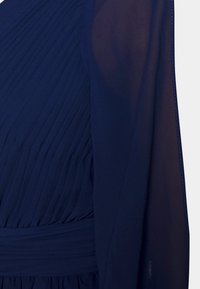 Navy-blaues Kleid mit plissiertem Design, das über lange, durchsichtige Ärmel und einen strukturierten Stoff verfügt. Die Taille wird mit einem breiten, glatten Band betont.