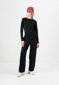 Black long-sleeve top and black sweatpants with an elastic waistband, paired with a pink cap. Sneakers in a light color. Simple, relaxed fit.