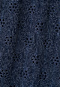 Tissu bleu marine avec un motif ondulé texturé et de petites formes de fleurs brodées composées de découpes carrées.