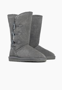 Stivali in suede grigi con punta arrotondata, caratterizzati da un design con lacci laterali con accessori grigi e una morbida fodera nella parte superiore. Suola piatta in gomma.