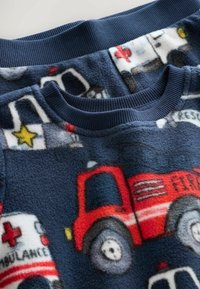 Fleecowa piżama górna w granatowym kolorze, ozdobiona kolorowymi wzorami z wozami strażackimi i ambulansami. Żebrowany granatowy kołnierz. Miękka tekstura.
