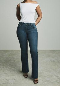 Jean en denim bleu foncé avec une coupe évasée, taille haute et poches avant. Associé à un haut ajusté blanc à épaules dénudées.