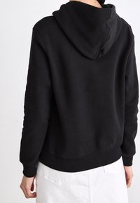 Černá mikina s kapucí z texturované látky, s žebrovanými manžetami a lemem a volným střihem. Na zádech nejsou žádné viditelné loga ani vzory.