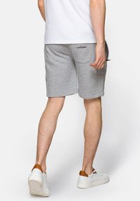 Szare sportowe spodenki o gładkiej teksturze, z bocznymi kieszeniami i wyhaftowanym logo. Noszone z białymi trampkami i prostą białą koszulą.