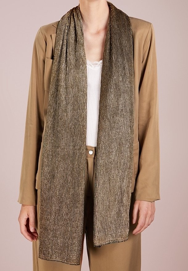 Longue écharpe côtelée bronze métallique portée sur un blazer beige et un haut blanc bordé de dentelle, montrée des épaules aux hanches.
