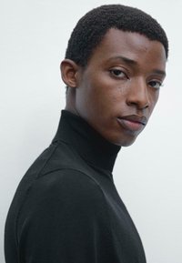 Black turtleneck sweater featuring a smooth texture, slim fit, and a high neck. The model is positioned in profile against a neutral background.