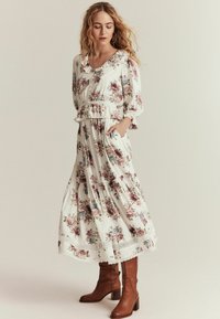 Blomstrete maxikjole med blonder i creme, med 3/4 ærmer og elastisk liv. Kombineret med brune knælange støvler.