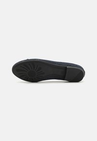 Semelle noire d'une chaussure avec un motif floral texturé. La tige présente un motif tacheté bleu foncé, un profil plat et aucun matériel visible.