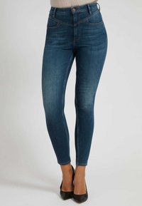 Tajta jeans i mörkblå denim, med hög midja, fem fickor och kontrasterande sömmar. Slät textur med lätt blekning.
