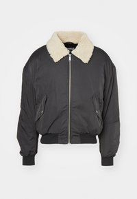 Chaqueta bomber negra con cuello de pelo sintético, cierre zip frontal, puños y dobladillo acanalados, y bolsillos laterales; tejido texturizado, corte relajado.