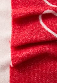 Tissu rouge avec une surface douce et texturée, présentant un léger dégradé avec une accentuation blanche. Les plis créent de la profondeur et de l'intérêt visuel.