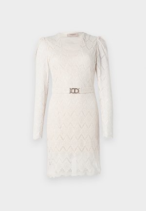 Spidsblondekjole i off-white med lange ærmer, V-udskæring og et mønster. Har et sølvfarvet bælte i taljen som accent.