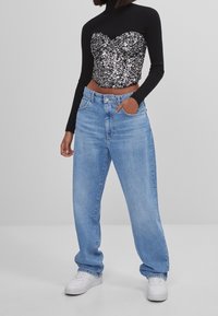 Svart långärmad topp med design av paljettbesatt bustier, kombinerad med ljusblå vida jeans och vita sneakers.