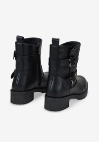 Botines negros de cuero suave con cremalleras laterales, dos hebillas decorativas y suelas de goma texturizadas. Tacones cortos apilados.