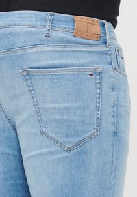 Light blue denim jeans featuring a leather patch labeled "Tommy Jeans," with a single back pocket and subtle stitching details.