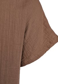 Brown, textured fabric with a wavy, raw-edge sleeve hem. The material appears lightweight and slightly crinkled.