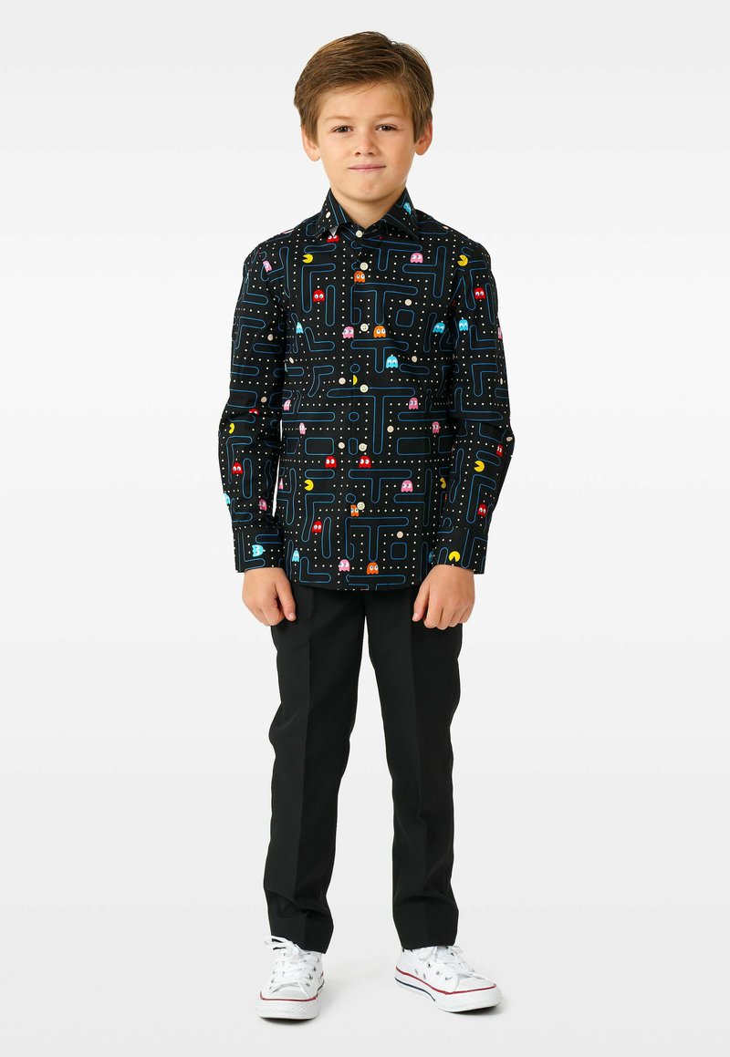 Čierna košeľa na gombíky s farebným vzorom Pac-Mana, dlhými rukávmi a klasickým golierom. Skombinovaná s čiernymi nohavicami a bielymi teniskami.
