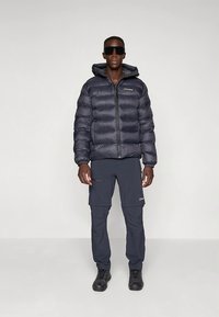 Puščavska jakna temno sive barve z zadrgo spredaj in pritrjeno kapuco. Kombinirana s temnimi cargo hlačami z žepi in logotipom. Črna obutev.