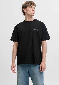 Sort bomulds T-shirt med rund hals og korte ærmer, der har et lille hvidt logo trykt på venstre side. Løs pasform.