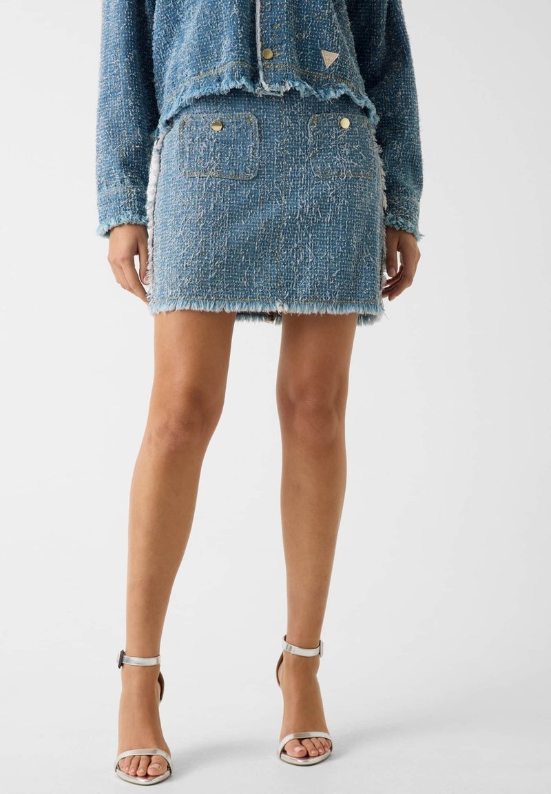 Completo in denim composto da giacca blu in tweed con frange e tasche, abbinata a una minigonna coordinata. Sandali argento con tacco alto completano il look.