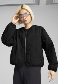 Schwarze gesteppte Jacke mit rundem Ausschnitt und durchgehendem Reißverschluss. Verfügt über weit geschnittene Ärmel und einen glatten, leicht strukturierten Stoff.