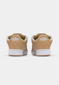 Sneaker Reebok con tomaia in suede beige, dettagli bianchi e logo sul tallone; presenta una suola in gomma e un collare imbottito.