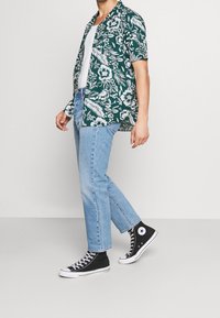 Vihreä kukallinen lyhythihainen paita, valkoinen toppi, vaaleansiniset suorat farkut ja mustat korkeavartiset tennarit valkoisilla yksityiskohdilla.