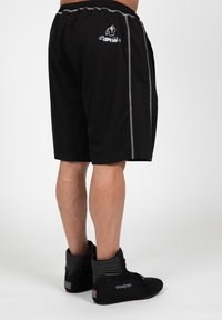 Zwarte sportshorts met een trekkoord in de taille, grijze zijaccenten en een logo aan de linkerkant. Gepaard met zwarte hoge sneakers.